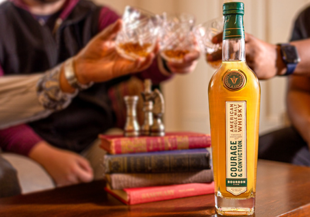Bottle of Virginia Distillery Company Whisky with hands holding glasses in the back